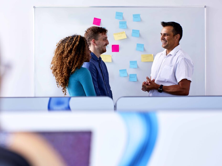 Three people stood in front of a whiteboard with post it notes on