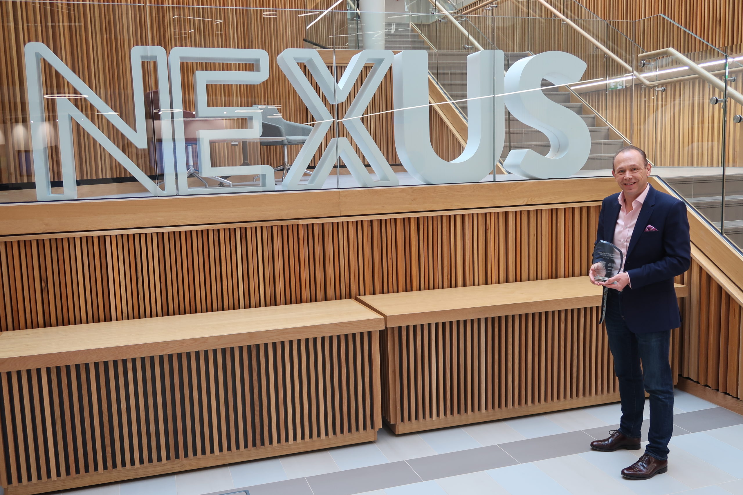 Dr Martin Stow (Nexus Director) standing in front of large Nexus logo holding a glass Leeds Digital Festival award trophy