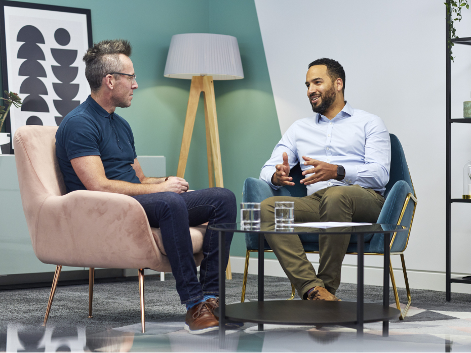Two men sat engaging in conversation at a coffee table.
