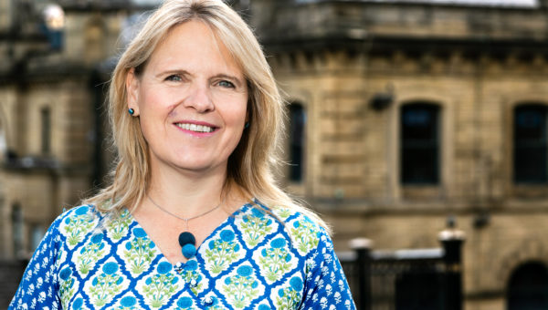 Head and shoulders shot of Kersten England, Chief Executive of Bradford Council. Kersten is stood facing camera and smiling with a building visible in the background.