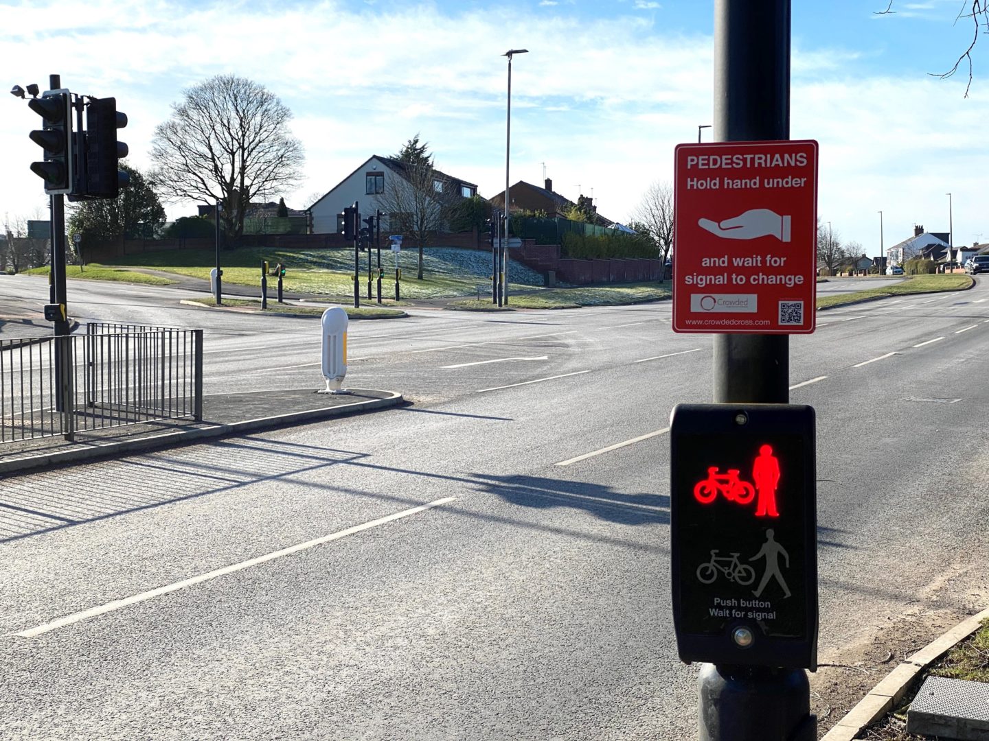 Image of pedestrian crossing signal box on red. Above is a sign for instructing users to wave their hand underneath to activate the signal box,