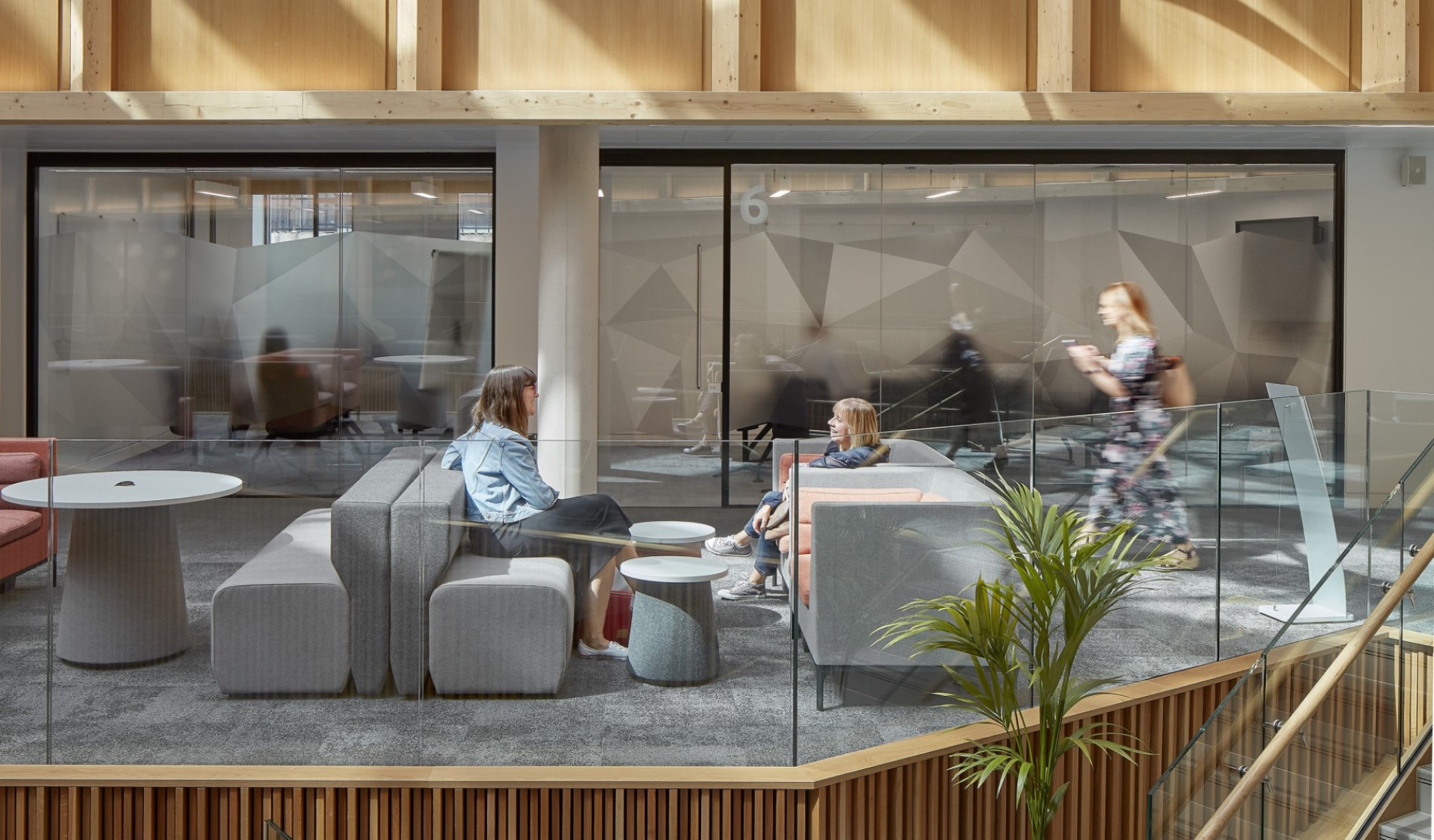 Two women sat on causal seating engaged in conversation as a third woman walks past