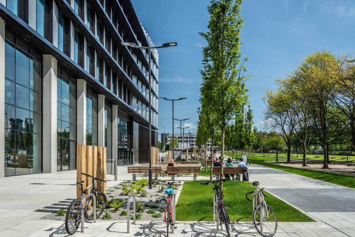 View looking down Discovery Way outside the Nexus building, the Nexus building can be seen on the left and bicycles and people sat on benches are in the foreground