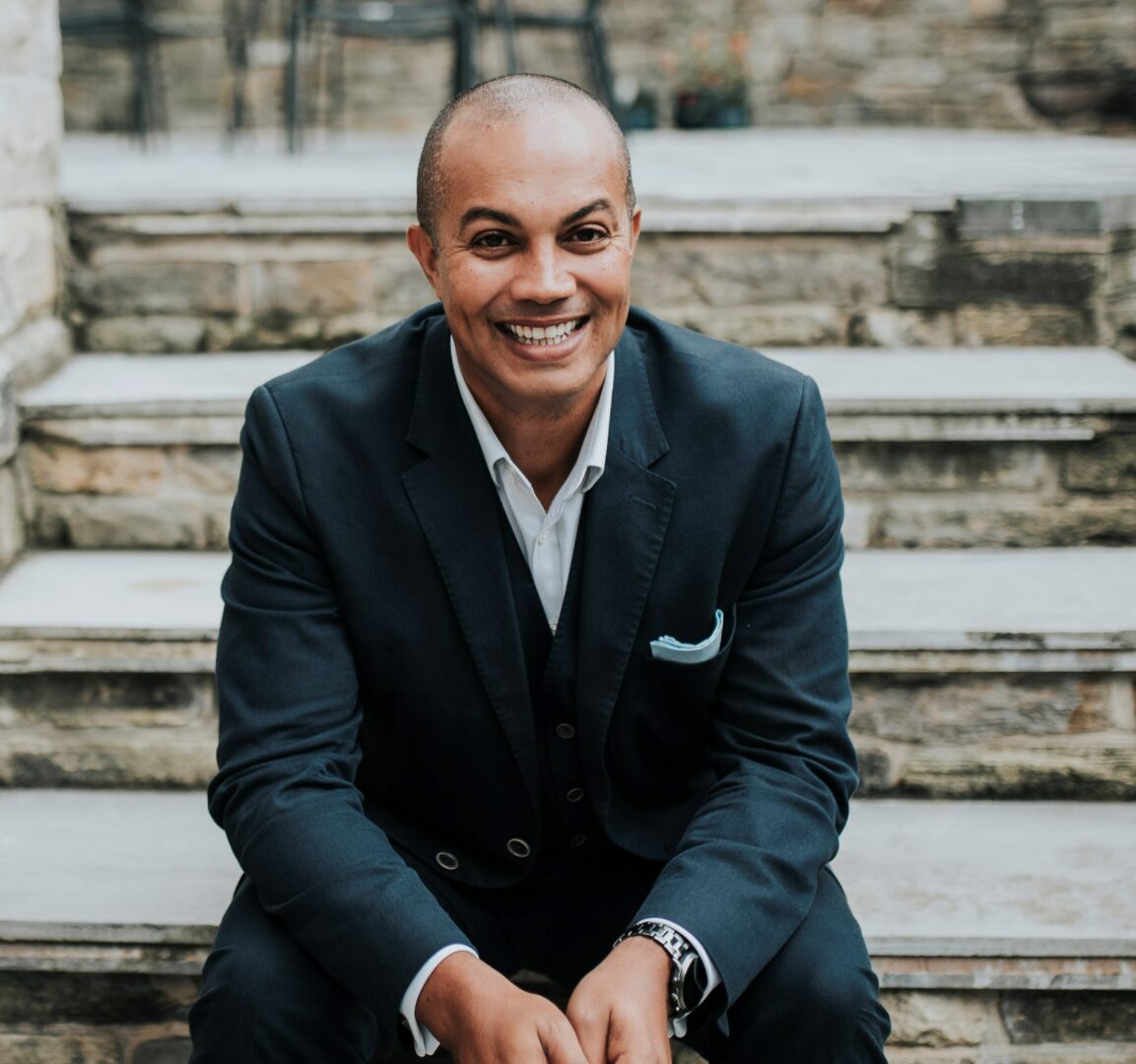 Man in a suit sits on steps and smiles at the camera