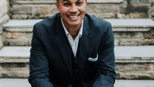 Man in a suit sits on steps and smiles at the camera