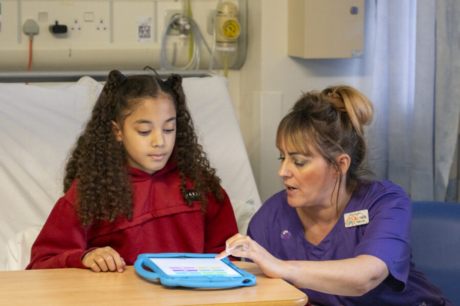 A young girl in hosiptal bed playing with the Little Journey application alongside a nurse.